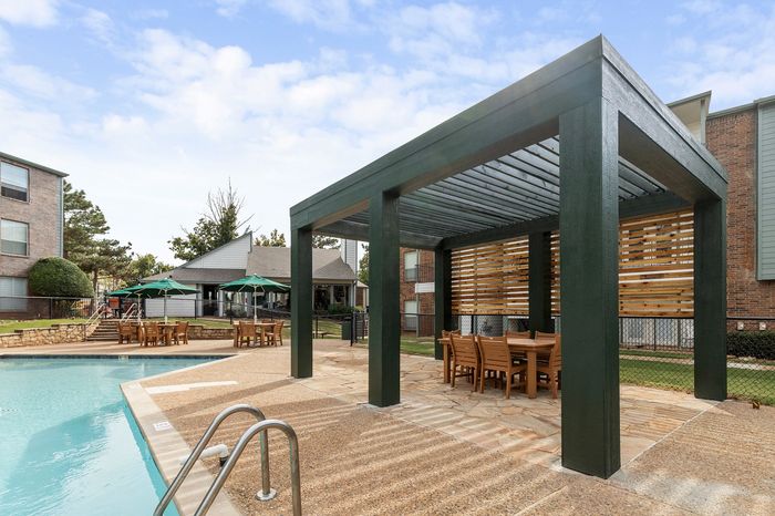 Charming apartment complex with inviting poolside pergola and outdoor dining area, perfect for relaxation and gatherings.