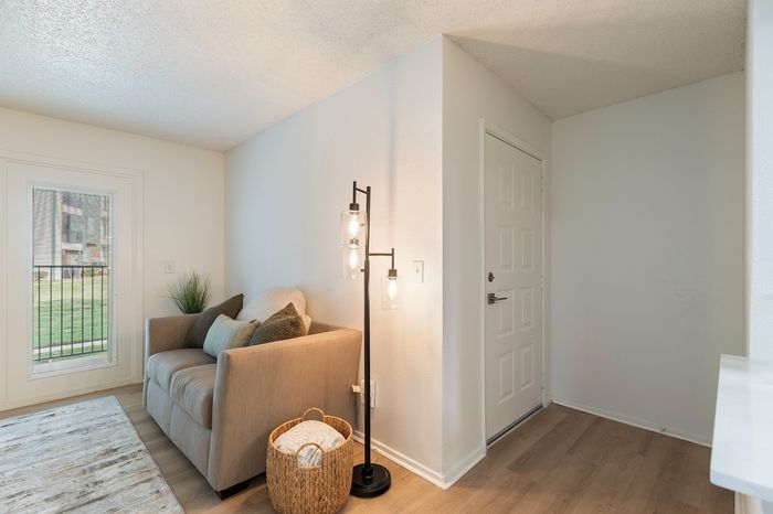 Cozy living space with a plush armchair, stylish floor lamp, and woven basket, complemented by natural light from a window view.
