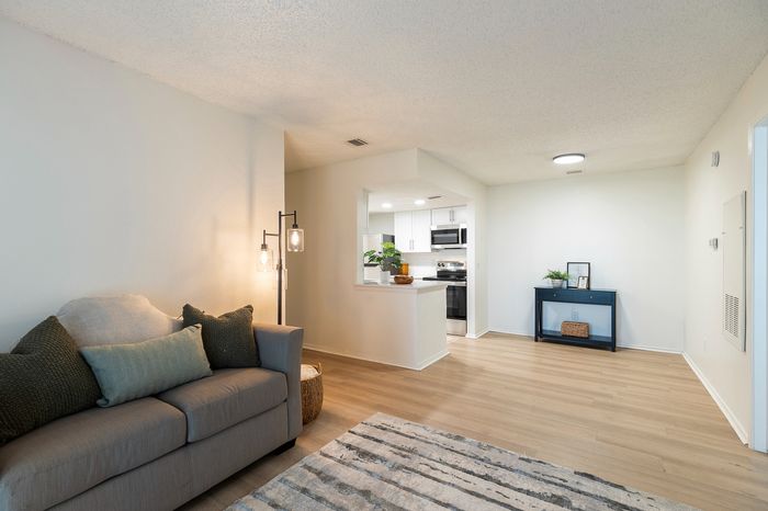 Inviting living room with modern sofa, elegant floor lamp, and seamless transition into a bright, stylish kitchen with stainless steel appliances.