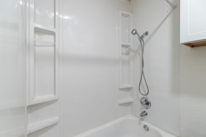 Modern white bathroom featuring a sleek showerhead and built-in shelving for a clean, minimalist look.