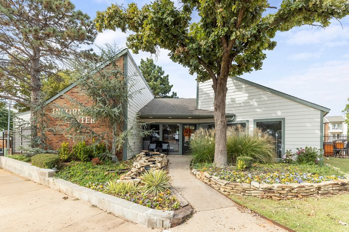 Charming apartment exterior with lush landscaping and inviting pathway, highlighted by vibrant flowers and mature trees.