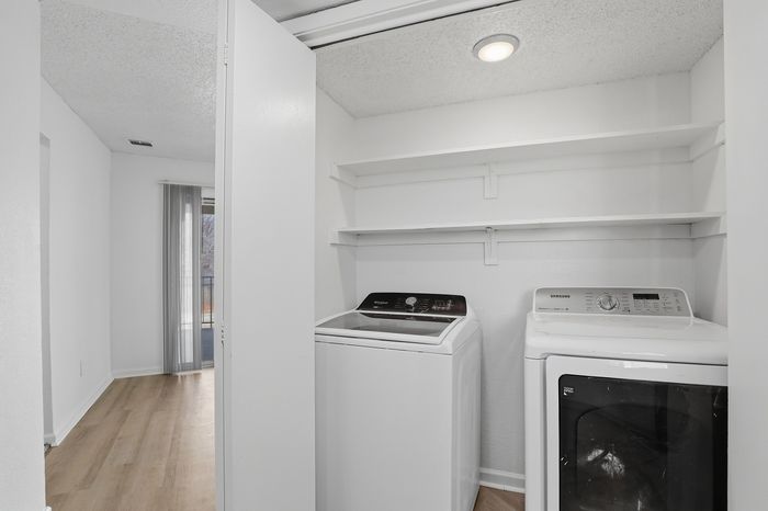 Bright laundry area featuring modern washer and dryer with convenient shelving in a stylish apartment.