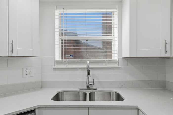 Bright and modern kitchen sink area with sleek stainless steel double sink, white cabinetry, and natural light streaming through the window.