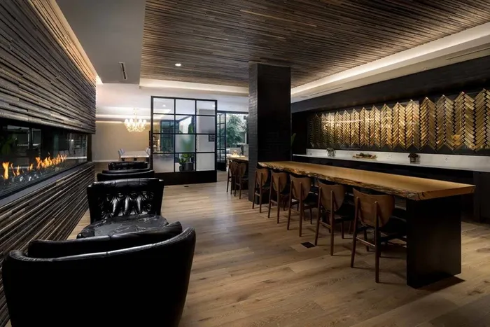 Club chairs near fireplace in front of long wooden gathering table and golden accents on the walls at Modera San Diego apartments.