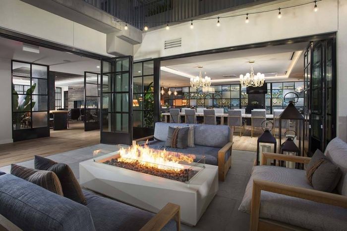 Closeup of fire table with lounge tables and indoor clubroom in the background at Modera San Diego apartments.