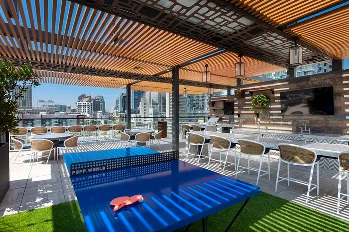 Ping pong table under shade structure in rooftop entertainment area looking out at the city at Modera San Diego apartments.