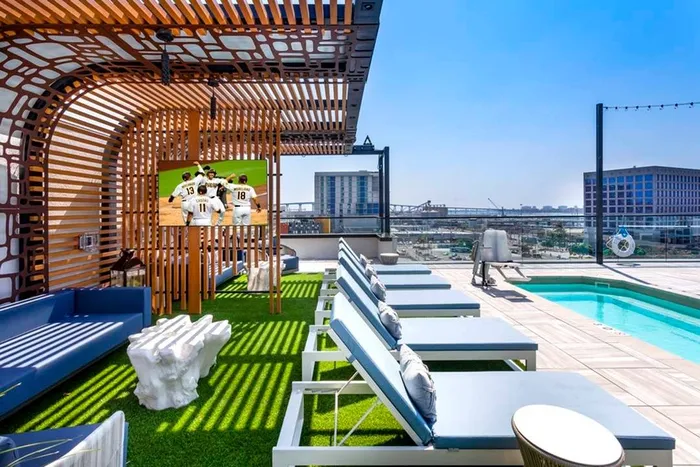 Lounge seating under shade structures with chaise lounge seating in the sun next to the rooftop pool at Modera San Diego apartments.