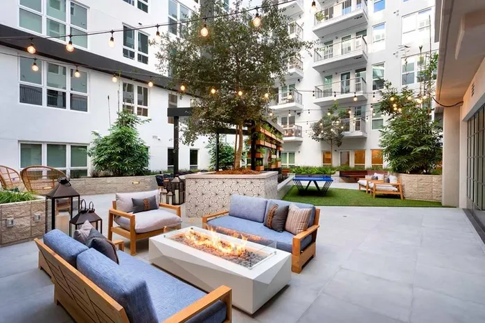 Firepit seating area under string lighting with outdoor kitchen and lounge area in the background at Modera San Diego apartments.