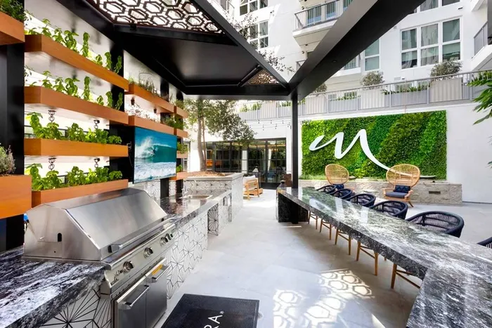 Outdoor courtyard kitchen entertainment area with grilling station, lush green landscaping, comfortable seating and outdoor TV at Modera San Diego apartments.