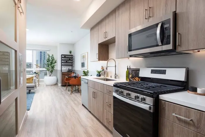 Sliding door to den or studio bedroom on the left with large windows in the living room beyond the galley-style kitchen at a Modera San Diego apartment.