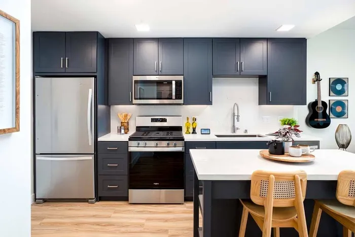 Kitchen at Modera San Diego with dark shaker-style cabinets, white quartz countertops, large chef's island with bar seating, gas range, stainless steel appliances and large basin sink with pull-down faucet