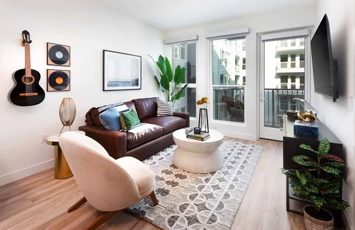 Living room at Modera San Diego with bohemian styling and an entertainment center with large windows and balcony on the courtyard in the background