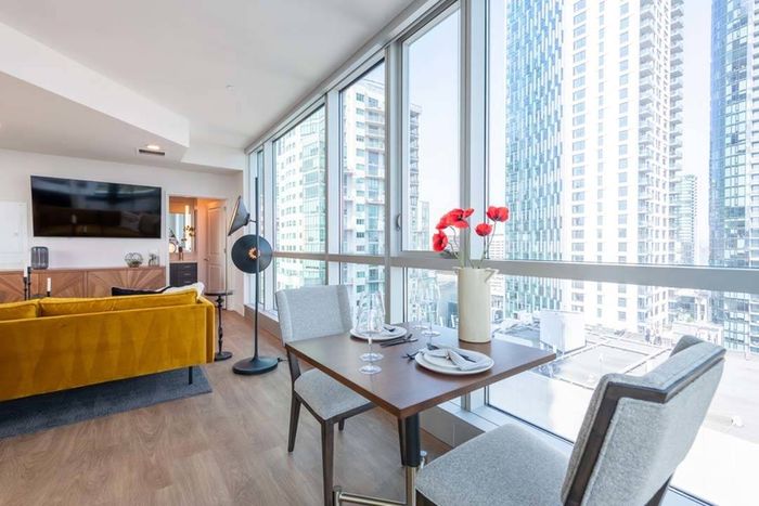 Table for two in front of glass walls that open to the city beyond with a couch and large TV in the background at Modera Rincon Hill apartments.