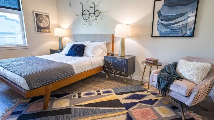 Furnished bedroom with queen bed, nightstand and chair