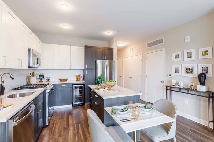 Two-toned kitchen cabinets with kitchen island and stainless steel appliances with wine cooler in background