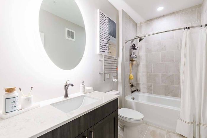 Round backlit bathroom mirrors with quartz countertops and tile surrounds