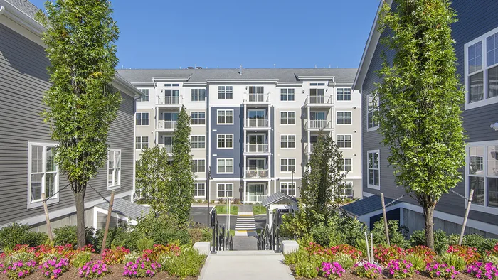 Cozy Location & Easy Living at Modera Needham - featuring beautiful landscaping with trees and flowers.