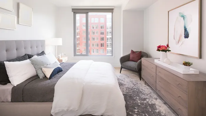 Bedroom with oversized window featuring queen bed, full size dresser, night stands, and an accent chair