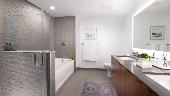 Large master bathroom with tile surround, dual vanity, dark quartz counter tops, and back lit vanity mirror
