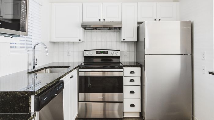 Brightly lit reimagined kitchen with dark granite countertops, stainless appliances, and light cabinetry