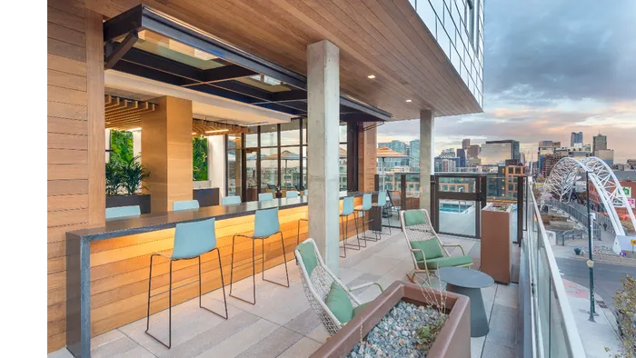 Indoor/outdoor lounge area with bar-style seating, garage-style door opening, kitchen, and flat screen TVs