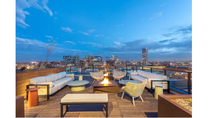 Rooftop terrace with a firepit, green spaces, and modern lounge seating facing stunning city views