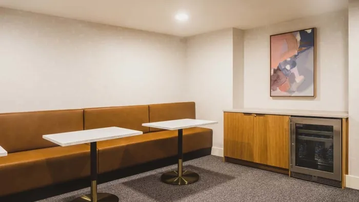 Two tables with banquette-style seating, small fridge, and artwork at Modera Broadway apartments.