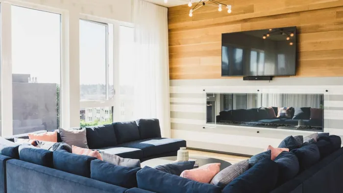 HDTV on the wall above a glass-walled fireplace with plush seating and city views at Modera Broadway apartments.