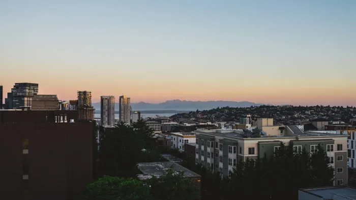 Mountains in the distance illuminated by an orange sunset over the city of Seattle