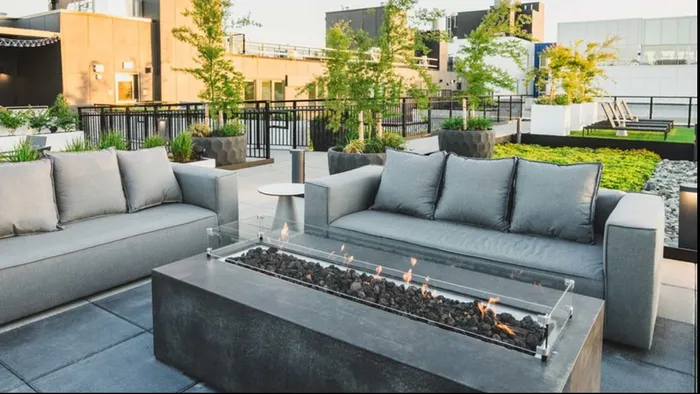 Fire pit lit up in front of 2 grey couches surrounded by greenery installations on the rooftop at Modera Broadway apartments.