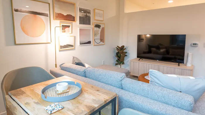 Small dining area within living space that features grey sofa and large HDTV on entertainment center in a Modera Broadway apartment.
