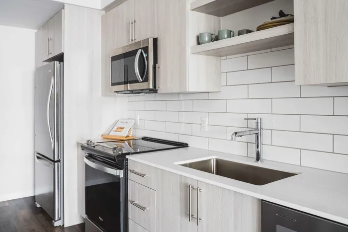Modera Coral Springs | Vacant kitchen with light cabinets, stainless appliances, quartz counters and dark wood-plank style floors