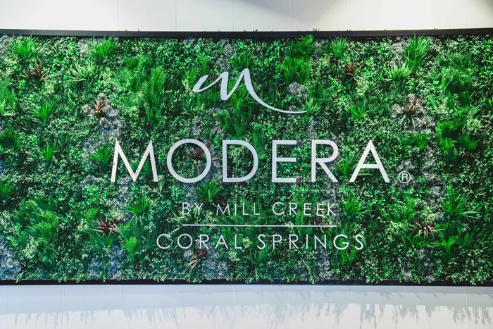 Modera Coral Springs apartments sign in front of faux greenery wall