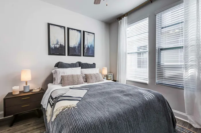 Large bedroom with cozy bed covered in gray cozy bedding with a large window in the background