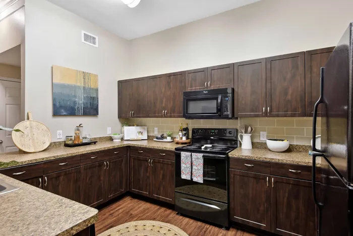 dark cabinetry in large kitchen with wood floors and black appliances alister sunset valley apartment homes for rent in austin tx