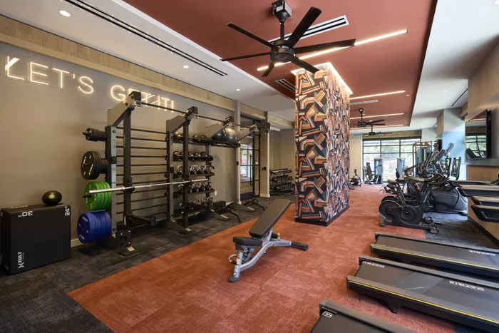fitness center with large ceiling fan, squat racks and red and brown flooring