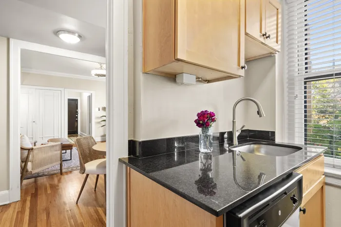 Charming kitchen corner with sleek black countertops and vibrant flowers, overlooking a cozy living space with elegant wooden flooring.