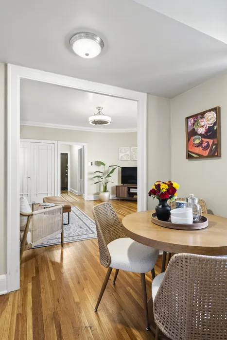 Inviting open living space showcasing elegant hardwood floors, a cozy dining area with woven chairs, and a bright, airy living room adorned with modern decor and vibrant floral accents.