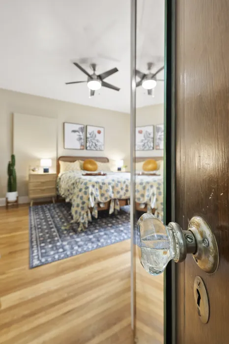 Inviting bedroom with elegant decor, featuring a cozy bed with patterned bedding, mirrored closet doors, and warm wooden flooring.