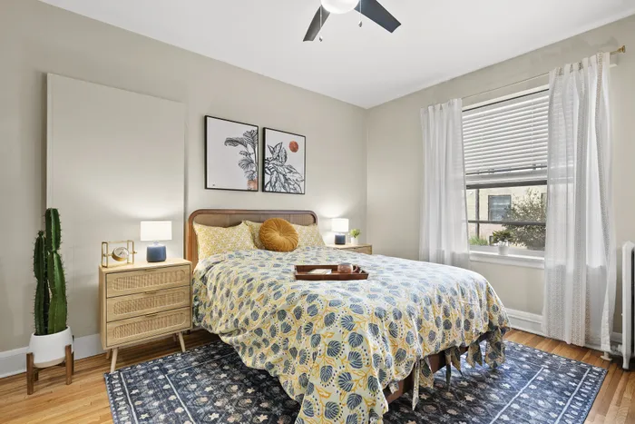 Bright and welcoming bedroom with stylish decor, featuring a cozy bed with patterned bedding, elegant wall art, and a sunlit window with flowing curtains.