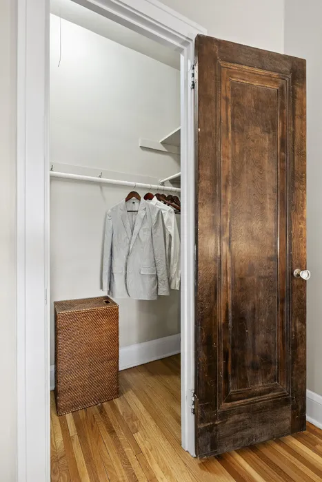 Elegant walk-in closet with wooden doors, showcasing sleek organization, wooden hangers, and a woven laundry hamper, offering a sophisticated storage solution.