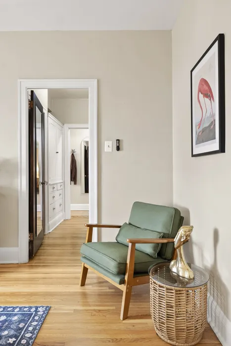 Inviting hallway view with a stylish green armchair, chic wicker side table, and elegant flamingo artwork.