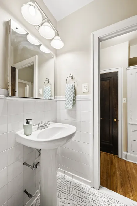 Bright, modern bathroom with a sleek white pedestal sink, elegant lighting, and stylish hexagonal floor tiles.