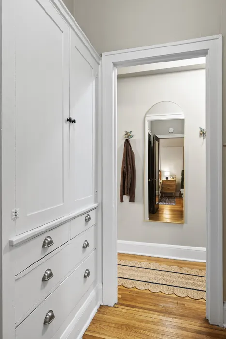 Cozy hallway with elegant white cabinetry and a stylish mirror reflecting a warm bedroom ambiance.