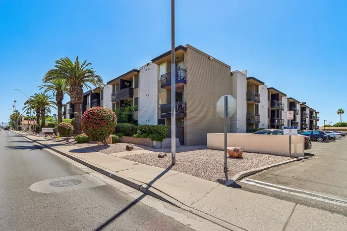 Charming apartment complex with modern architecture, featuring palm trees and vibrant landscaping under a clear blue sky.