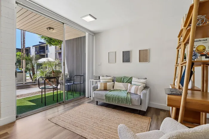 Charming apartment living area with cozy sofa, modern decor, and expansive glass doors opening to a lush garden view.