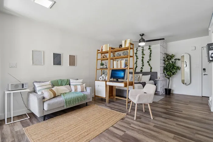 Chic apartment interior with modern decor features a cozy sofa, stylish open shelving, and a serene bedroom area with lush greenery.
