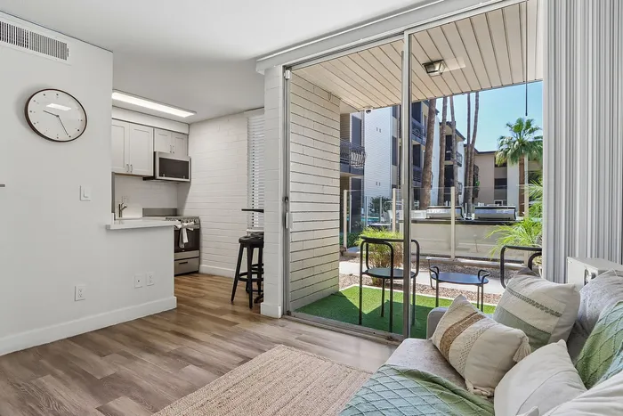 Bright and modern apartment with open living space, stylish kitchen, and a cozy patio view featuring lush greenery.