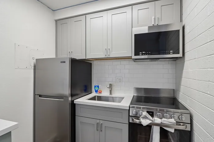 Modern compact kitchen with sleek stainless steel appliances, subway tile backsplash, and elegant gray cabinets.