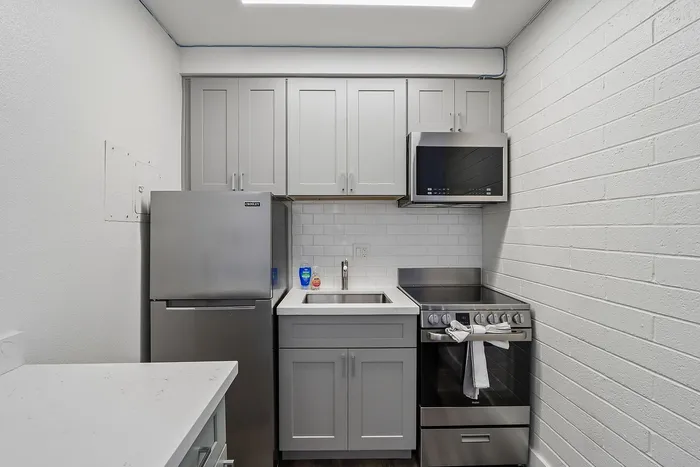 Contemporary kitchen with sleek stainless steel appliances, elegant gray cabinetry, and a polished white countertop.
